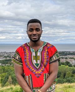 Photo of Billy Byiringiro wearing a bright-coloured top, stood outside.